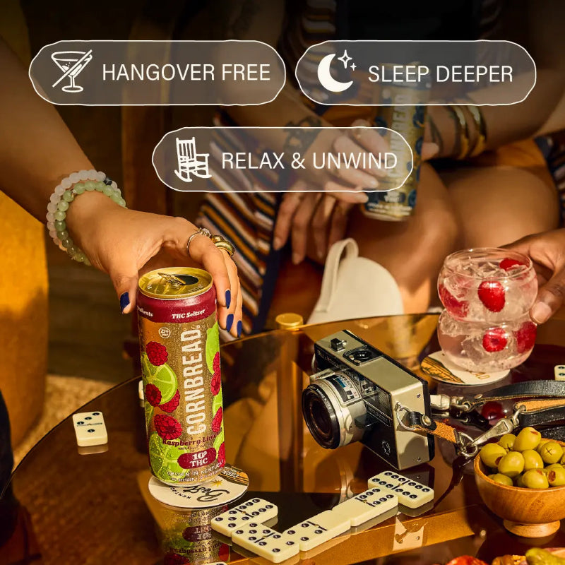 Person holding a can of cornbread cocktail with text about its benefits, on a table with a camera and snacks.