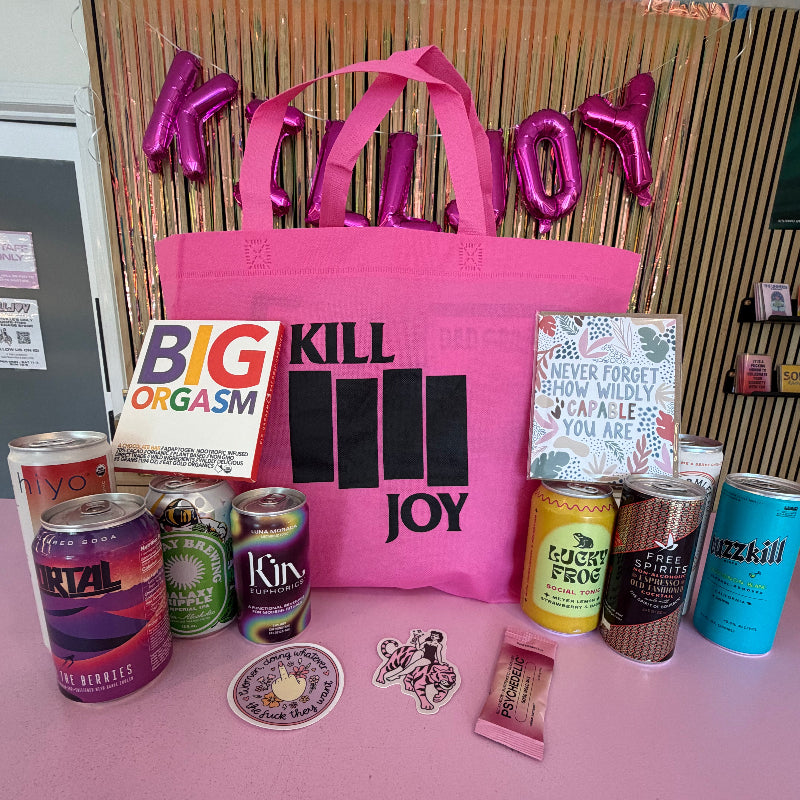 Pink tote bag with 'Kill Joy' text, various items including cans and a book on a pink surface.