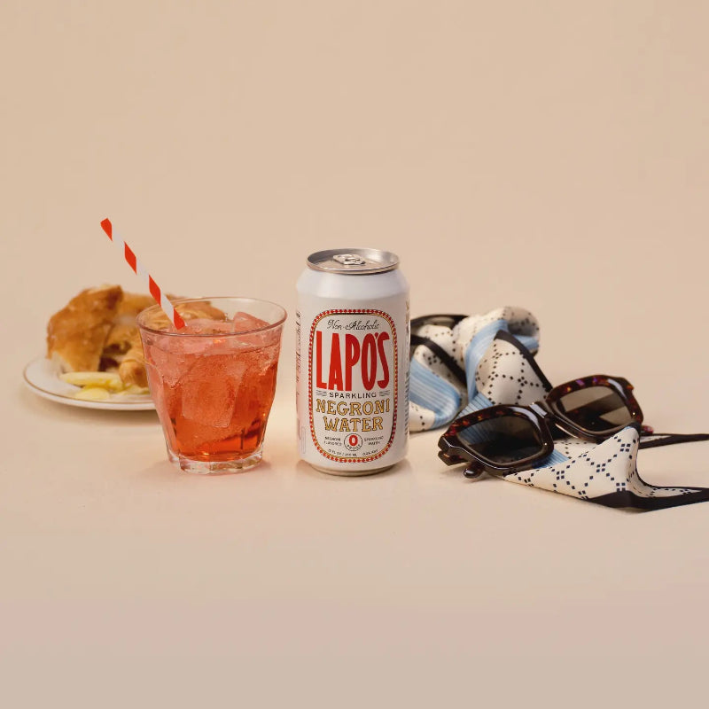 Can of Lapos Negromi Water with a glass of red drink and sunglasses on a beige background