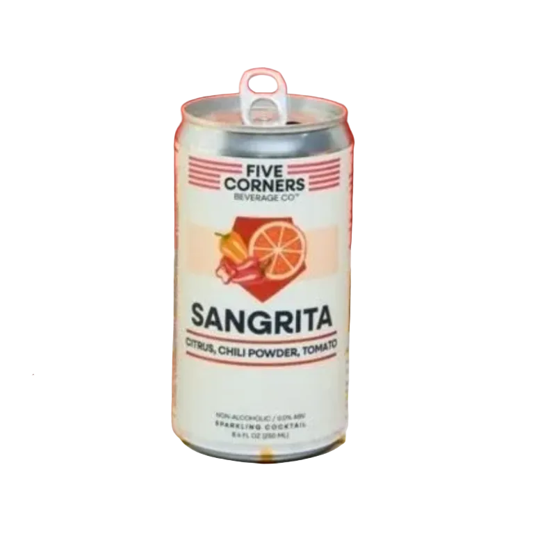 A can of Five Corners Sangrita sparkling cocktail mix stands on a white tiled counter with yellow grid lines. The can is white with red and orange graphics, surrounded by a basket of lime and red chili peppers on the left, and a glass of orange-colored drink with a lime wedge on the right, against a solid red background.