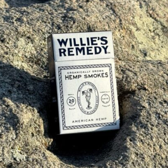 A pack of Willie's Remedy Hemp Smokes resting on a textured gray rock outdoors.