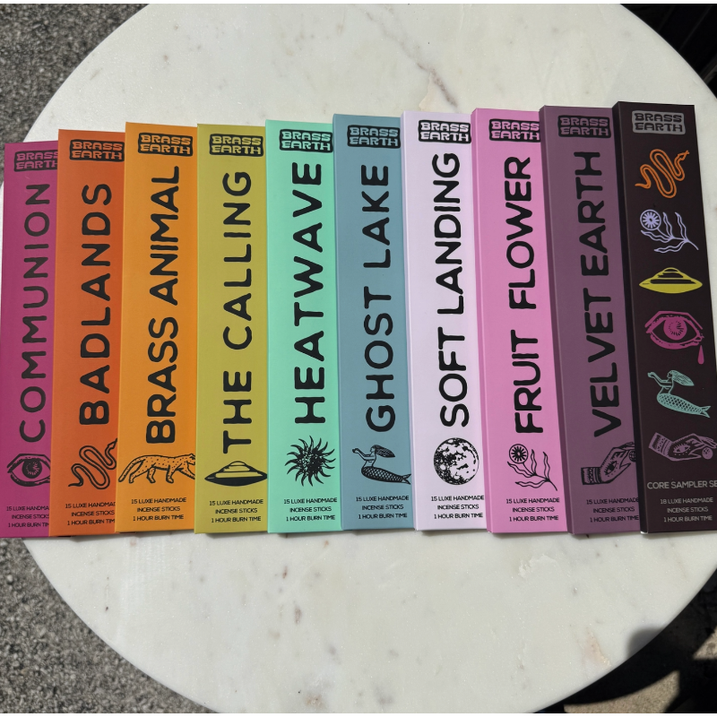 A set of ten colorful Brass Earth vinyl record sleeve covers arranged in a fan shape on a white marble surface. The sleeves feature different illustrated designs and titles including Communion, Badlands, The Calling, Heatwave, Ghost Lake, Soft Landing, Fruit Flower, Velvet Earth, and Cone Sampler Set.