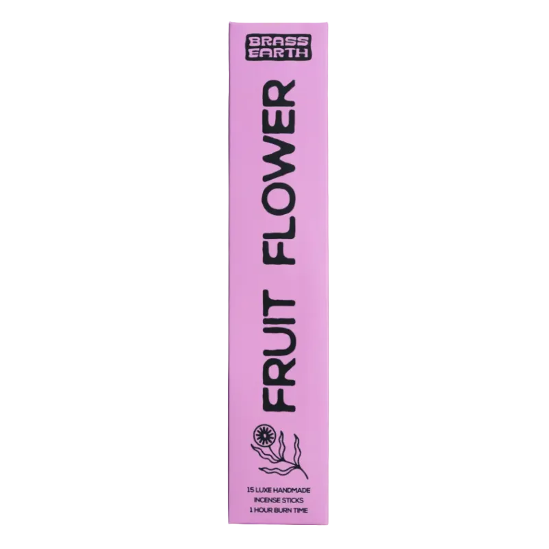 A tall, narrow pink box for Grass Earth Fruit Flower incense sticks stands upright against a solid lavender background. The packaging features bold black text and a simple line drawing of a flower.
